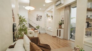A modern living room with a sofa, a dining area, a staircase, and a large window. - Là Home - Stay Cozy, Stay Home Phú Nhuận (Ho Chi Minh City)