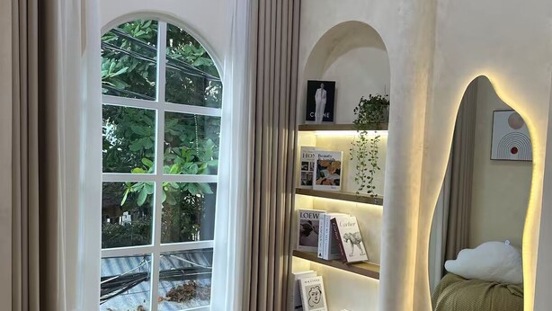 A modern bedroom with a large window, a cozy reading chair, a built-in bookshelf, and a mirror with integrated lighting. - Là Home - Stay Cozy, Stay Home Phú Nhuận (Ho Chi Minh City)
