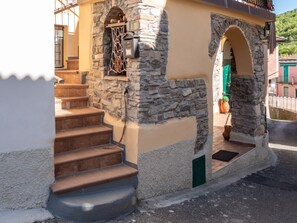 A stone staircase leading to a door with a green door frame, a small window with a decorative metal grille, and a potted plant on the ground. - Rosano 76 - 5 minutes from Cabella Ligure (Rosano)