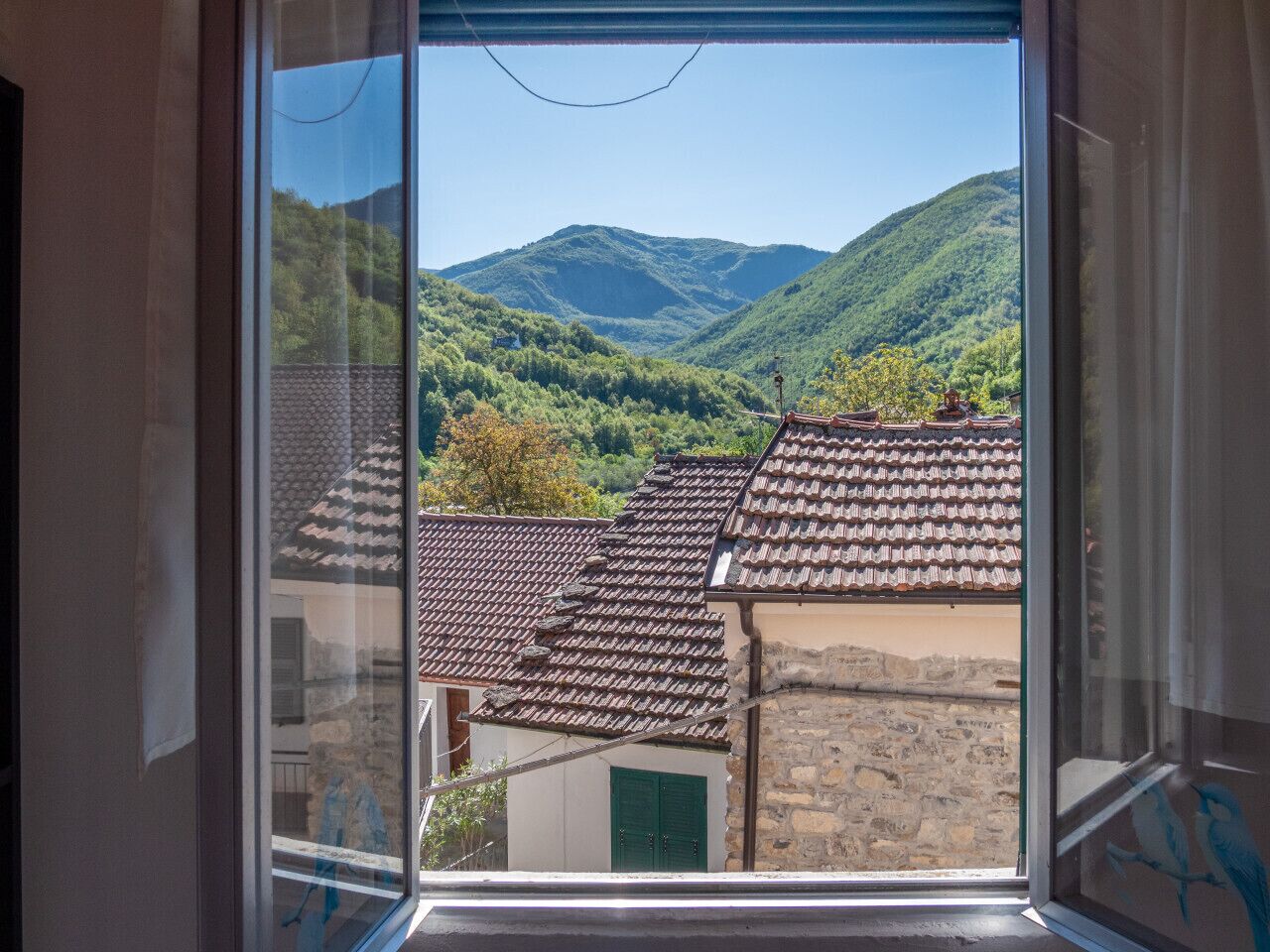 Une vue par la fenêtre sur un paysage montagneux, avec des toits traditionnels en tuiles et des bâtiments en pierre.