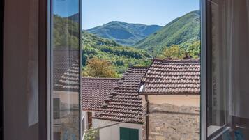 Une vue par la fenêtre sur un paysage montagneux, avec des toits traditionnels en tuiles et des bâtiments en pierre.