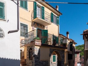 A two-story building with a stone archway entrance, a balcony with green shutters, and a clear blue sky. - Rosano 76 - 5 minutes from Cabella Ligure (Rosano)