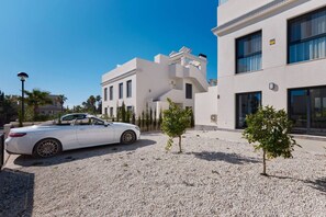 A white convertible car parked in a gravel driveway with a modern building in the background. - Rojales Poolside Apartment (Quesada)