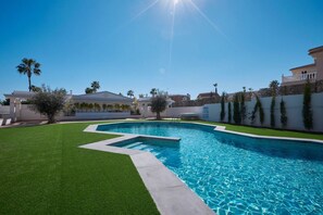 A swimming pool with a clear blue water, surrounded by a well-maintained lawn and a white wall. - Rojales Poolside Apartment (Quesada)
