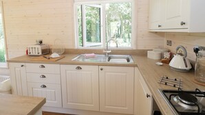 A kitchen with wooden cabinets, a window, a sink, a toaster, a kettle, and a stove. - Skylark (Ross-on-Wye)