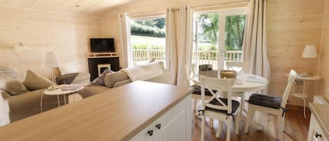 A cozy cabin interior with a wooden ceiling, a sofa, a TV, a dining table with chairs, and a fireplace.