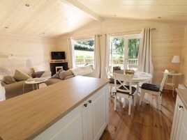 Interior acolhedor de uma cabana com teto de madeira, um sofá, uma televisão, uma mesa de jantar com cadeiras e uma lareira.