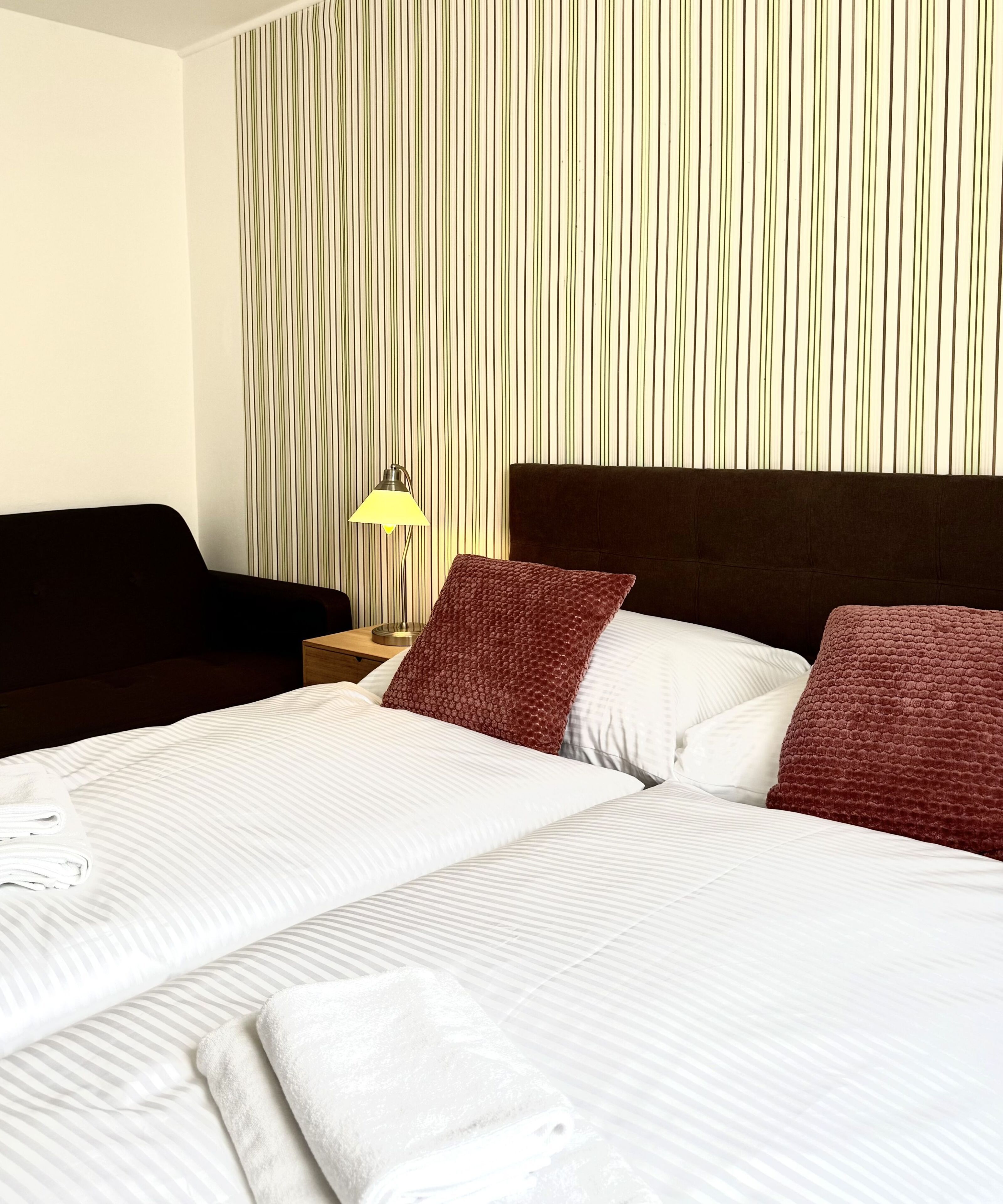 A neatly made bed with white linens, a brown headboard, and two red pillows.