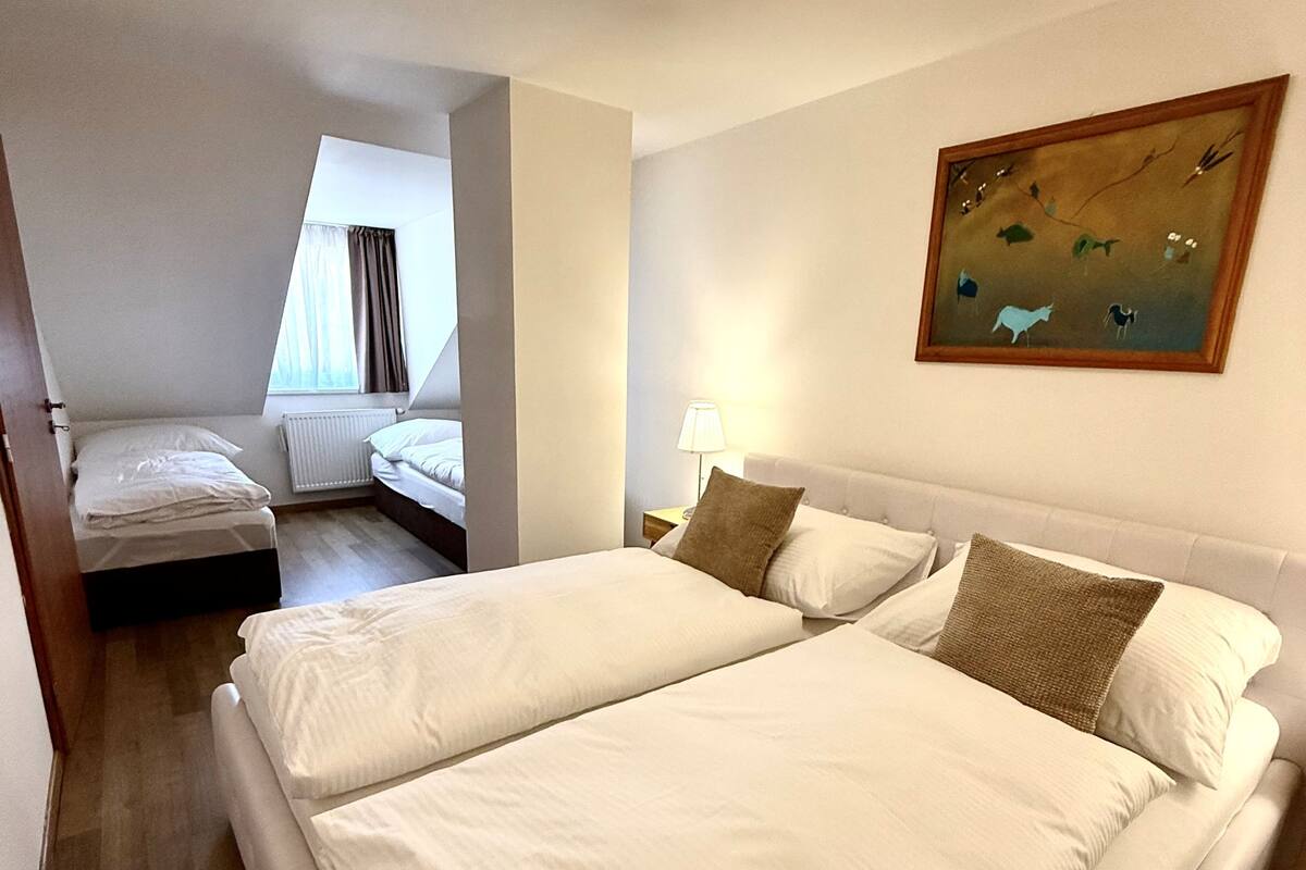 Una habitación de hotel con una cama grande, una cama más pequeña, un cuadro y una lámpara en el techo.