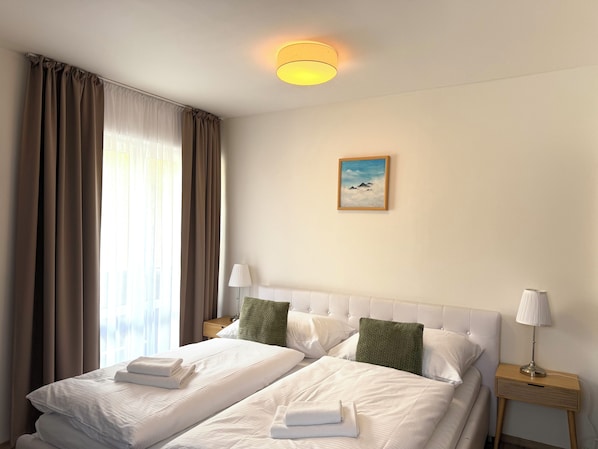 A hotel room with two beds, a painting on the wall, and a nightstand with a lamp.