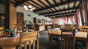 A restaurant with wooden tables and chairs, a stone wall, and a fireplace. - Penzión a reštaurácia Raimund (Vysoké Tatry)