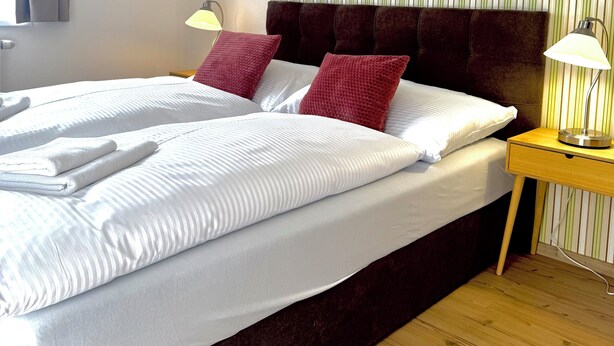 A hotel room with a large bed, two bedside lamps, a striped wall, and a wooden floor. - Penzión a reštaurácia Raimund (Vysoké Tatry)