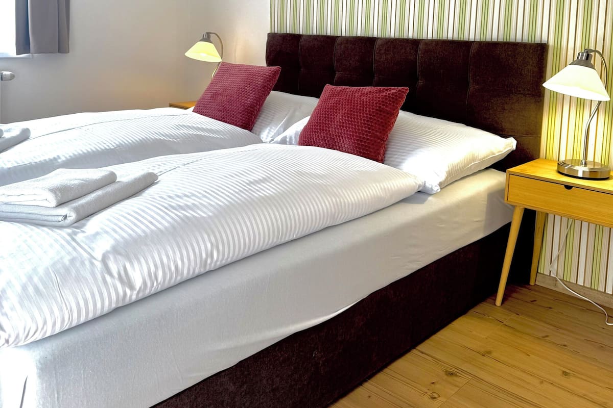 Una habitación de hotel con una cama grande, dos lámparas de noche, una pared a rayas y suelo de madera.