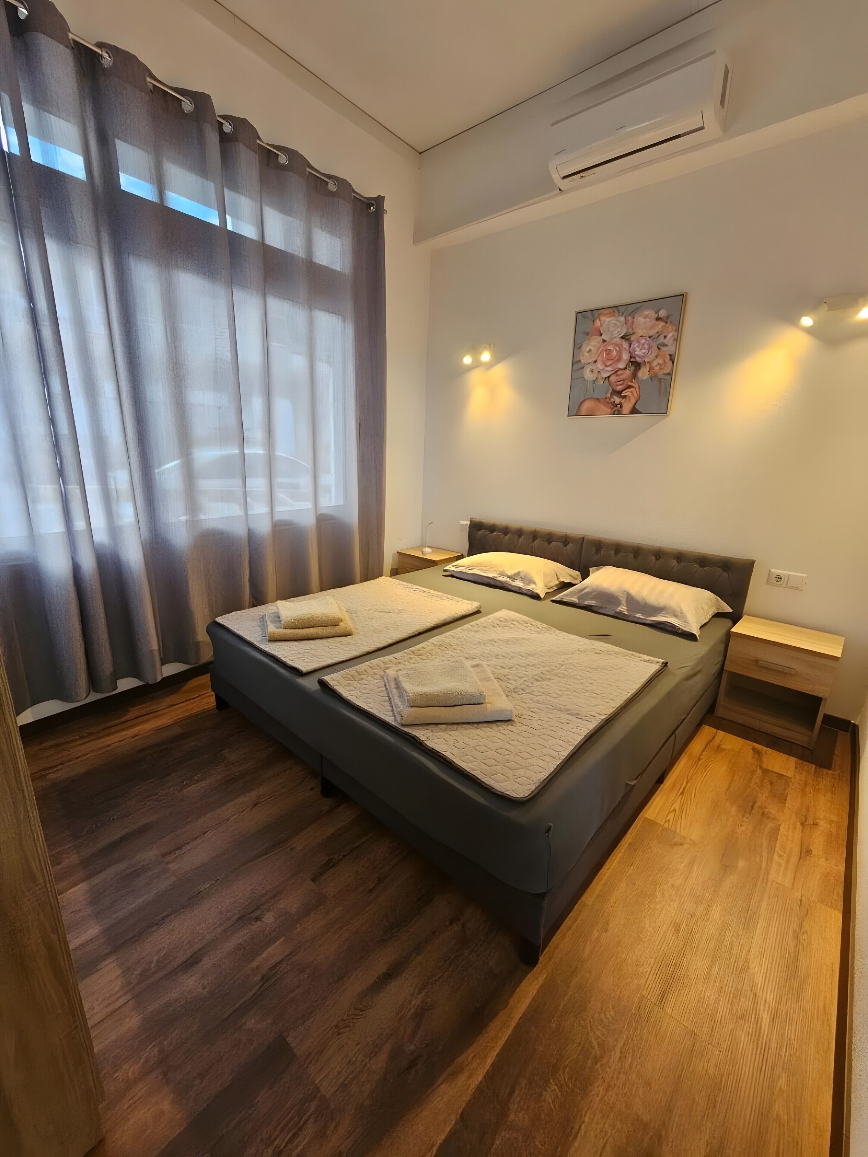 Een slaapkamer met een bed, gordijnen, een airconditioner, een nachtkastje en een wandlamp.