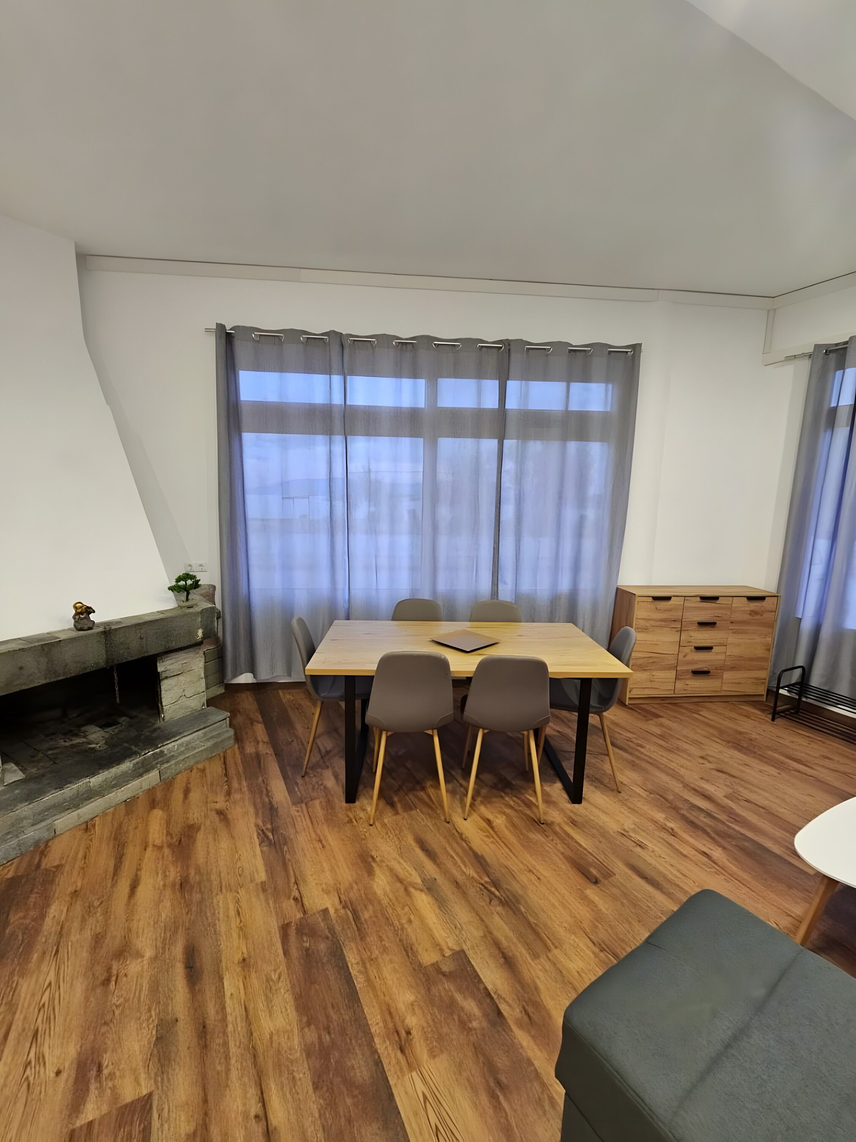A room with a wooden dining table, four chairs, a small plant, a wooden cabinet, and a fireplace.