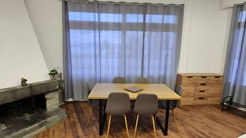 A room with a wooden dining table, four chairs, a small plant, a wooden cabinet, and a fireplace.