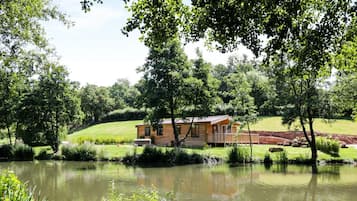 Una cabaña de madera junto a un lago, con una colina cubierta de pasto al fondo.