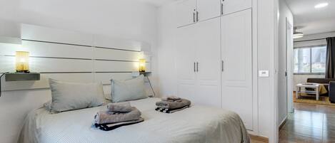 A modern bedroom with a large bed, a wardrobe, and a bedside table with lamps.