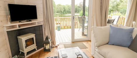 A cozy living room with a fireplace, a television, a sofa, and a view of a deck and greenery outside.