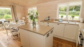 Una cocina moderna con armarios de madera, una isla central y una zona de comedor con sillas blancas.