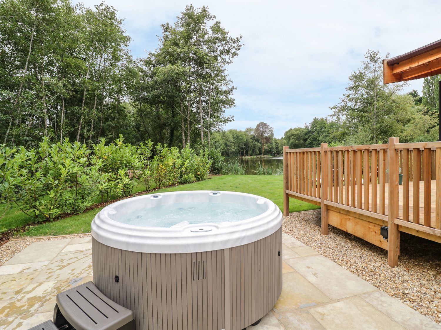 Un jacuzzi en un jardín con una terraza de madera y un estanque al fondo.