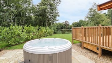 Un jacuzzi en un jardín con una terraza de madera y un estanque al fondo.