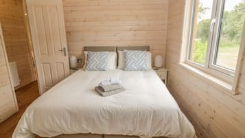 Un dormitorio con techo de madera, una cama grande con ropa de cama blanca, dos mesitas de noche y una ventana con vistas a la vegetación.