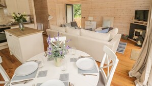 Interior acogedor de una cabaña con comedor, sofá, televisor y chimenea.
