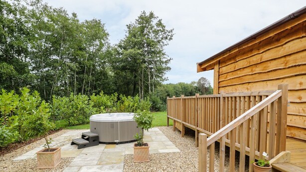 Un jacuzzi en un jardín con terraza de madera y escalones que llevan a una cabaña.