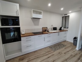 Une cuisine moderne avec des meubles blancs, un plan de travail en bois, un four à micro-ondes encastré, un grille-pain et un évier.