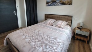 A bedroom with a bed, a painting, a nightstand, and a door.