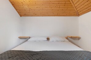 A bedroom with a wooden ceiling, a bed with white bedding, and two wooden bedside tables.