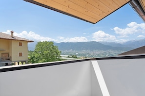 A balcony with a view of mountains, a tree, and a building.