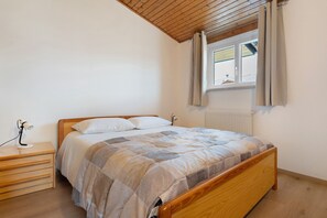 A bedroom with a wooden bed, a nightstand with a lamp, a window with curtains, and a view of the outside.