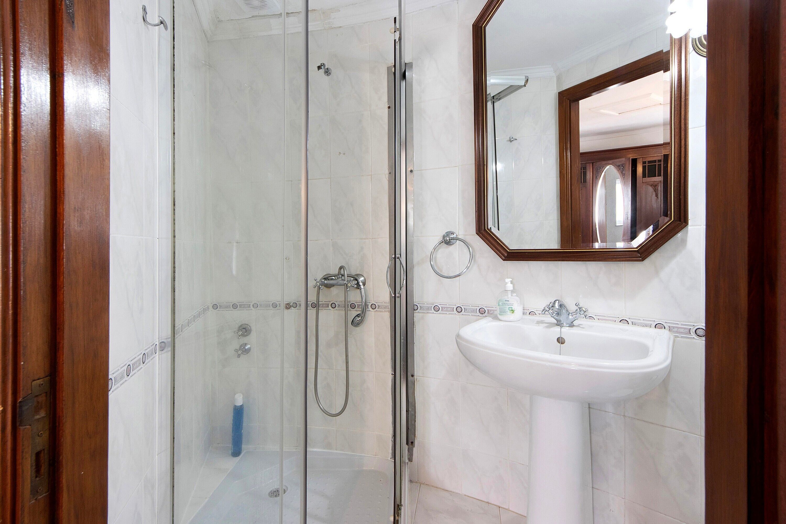 A bathroom with a glass-enclosed shower, a white sink, and a mirror.