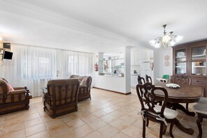 A dining area with a round table and chairs, a kitchen in the background, and a living room with sofas and a TV. - Holiday Home 'Moinho Velho' with Private Pool, Private Terrace and Wi-Fi (Cristelo)