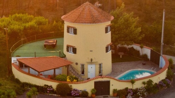 Ein kreisrunder Turm mit Swimmingpool, umgeben von Garten und bewaldetem Gelände.
