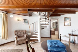 A room with a spiral staircase, a tufted armchair, a dining table with a blue tablecloth, and a wooden ceiling. - Holiday Home 'Moinho Velho' with Private Pool, Private Terrace and Wi-Fi (Cristelo)