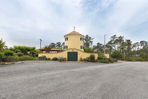 A single-story building with a round tower, a green door, and a gravel driveway. - Holiday Home 'Moinho Velho' with Private Pool, Private Terrace and Wi-Fi (Cristelo)