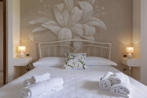 Quarto de hotel com um grande mural floral na parede, cama bem arrumada com roupa de cama branca e duas luminárias de cabeceira.