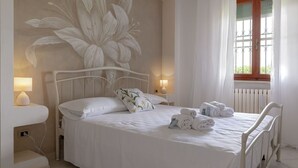 A bedroom with a large floral mural, a bed with white linens, two bedside lamps, and a window with curtains. - Giglio Pool & Nature 15 mins to Pisa | Domio (Cascina)