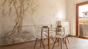 A dining area with a glass table, clear chairs, and a mural of trees on the wall.
