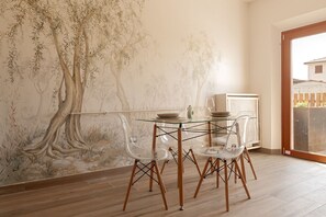 A dining area with a glass table, clear chairs, and a mural of trees on the wall. - Olivo: Pool & Nature 15 mins to Pisa | Domio (Cascina)