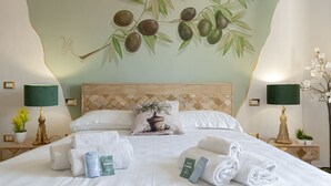 A hotel room with a bed, pillows, a headboard, a nightstand with a lamp, and a wall mural.