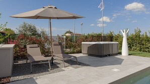 An outdoor patio with a pool, lounge chairs, an umbrella, and a hot tub.