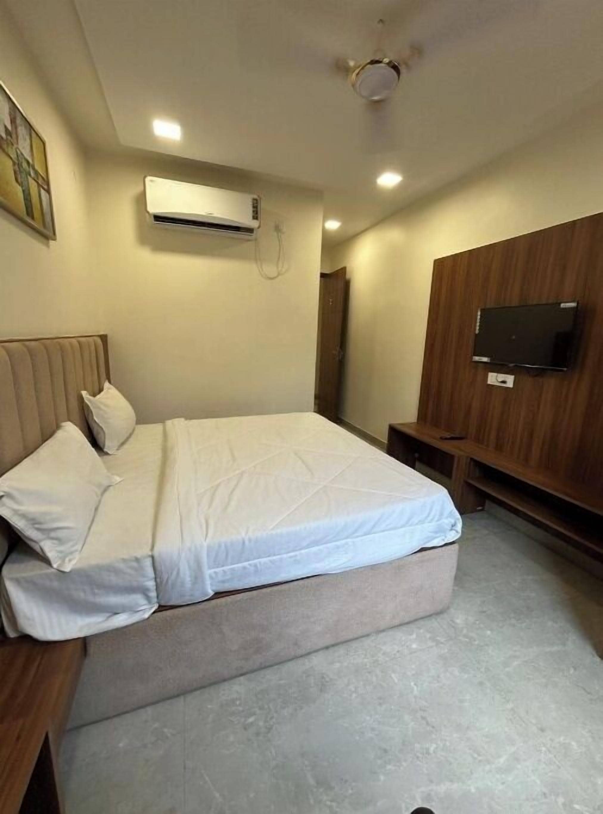 A bedroom with a bed, an air conditioning unit, a television, and a wooden panel wall.
