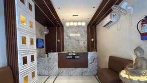 A reception area with a marble counter, a reception desk, a statue, and a wall-mounted air conditioning unit. - Namaste Haridwar By Oran Hotels (Haridwar)