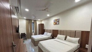 A hotel room with two beds, a desk, a chair, a wardrobe, and a ceiling fan. - Namaste Haridwar By Oran Hotels (Haridwar)