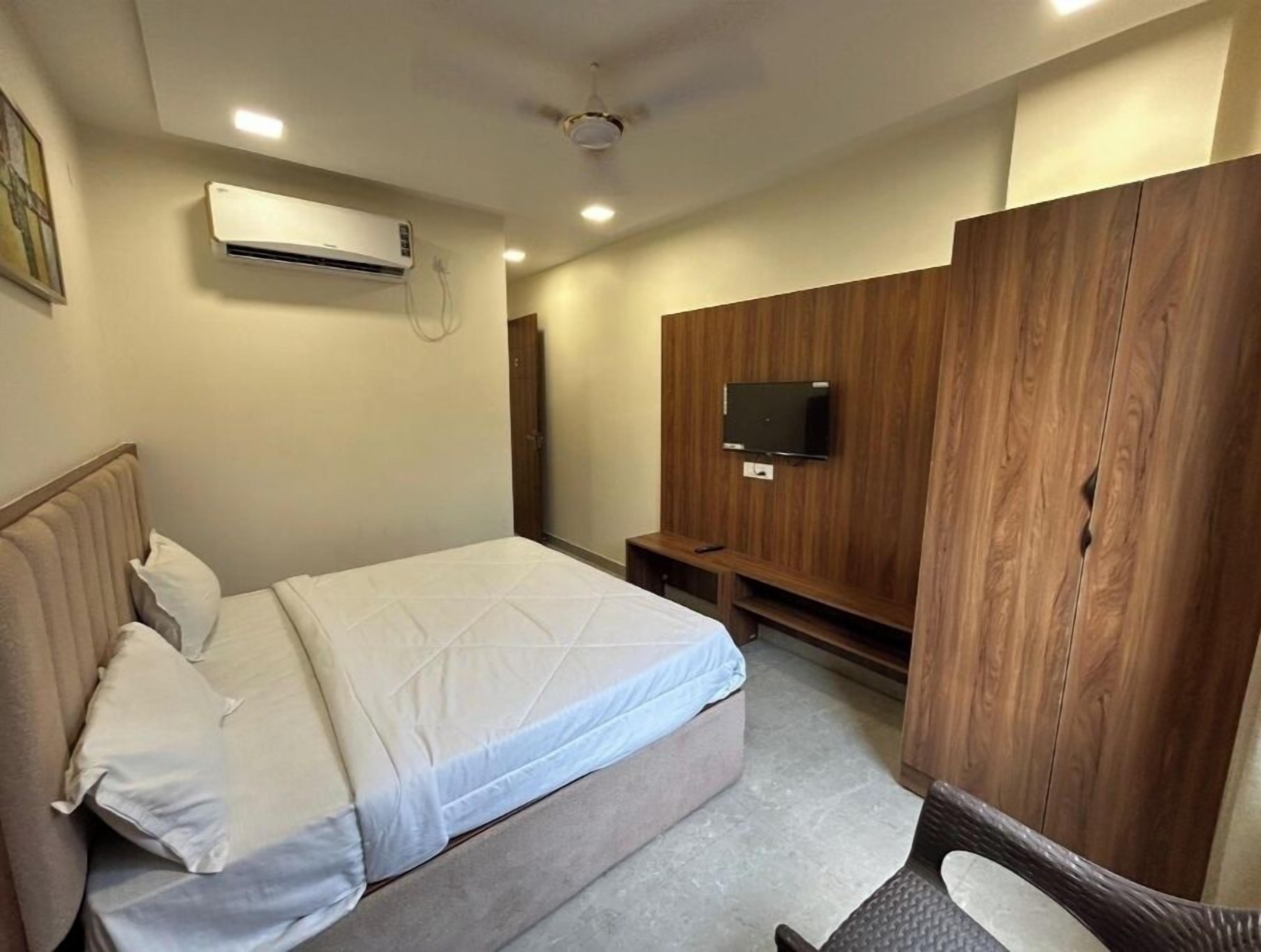 A bedroom with a bed, an air conditioning unit, a television on a wooden panel, and a ceiling fan.