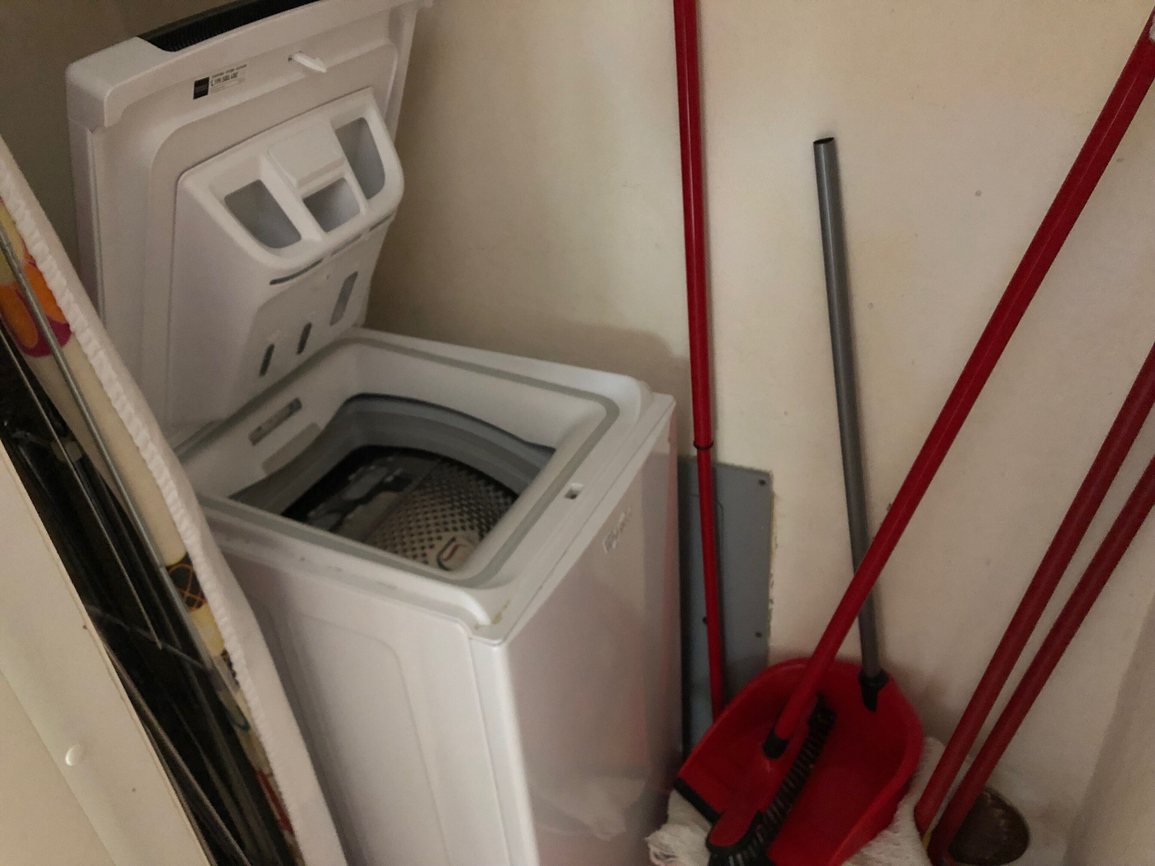 Een kleine wasruimte met een wasmachine, een dweil en een bezem.